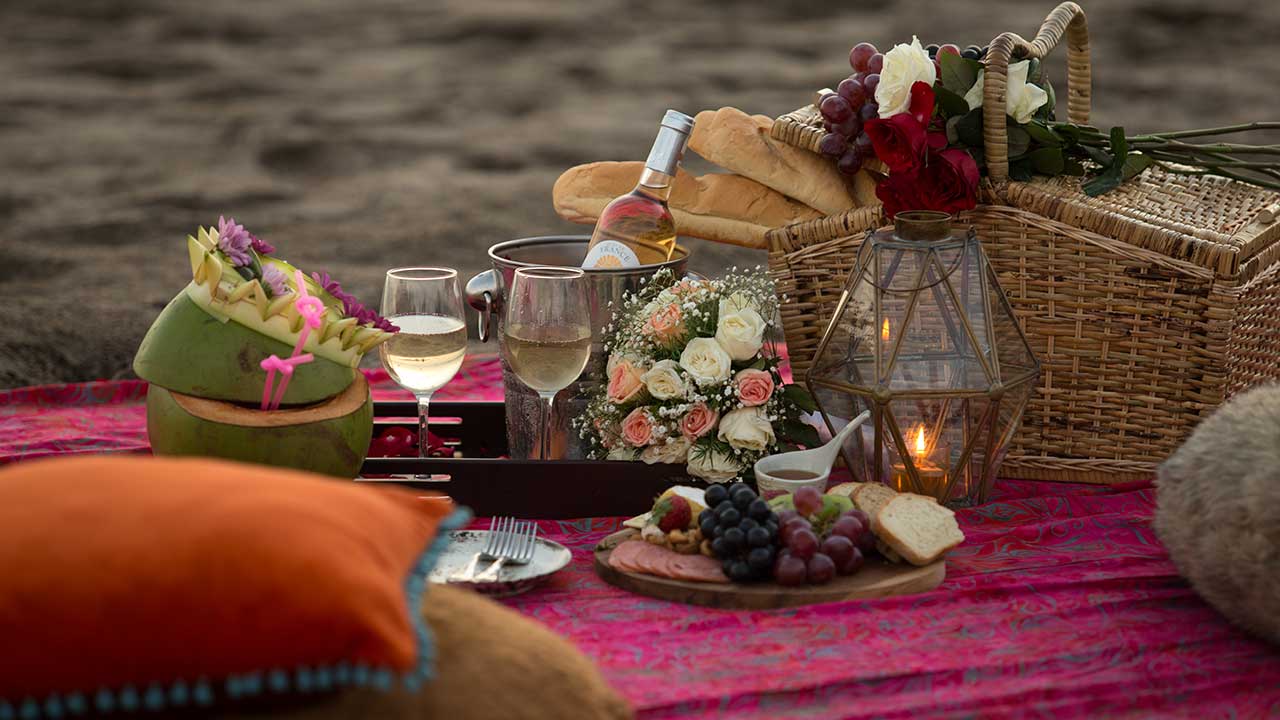 Setup de picnic romántico con mantel de lino, flores y canasta gourmet en un jardín de Puriscal