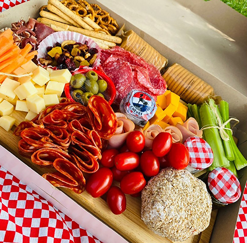 Canasta de mimbre con quesos artesanales, frutas, panes y vino sobre fondo de lino natural